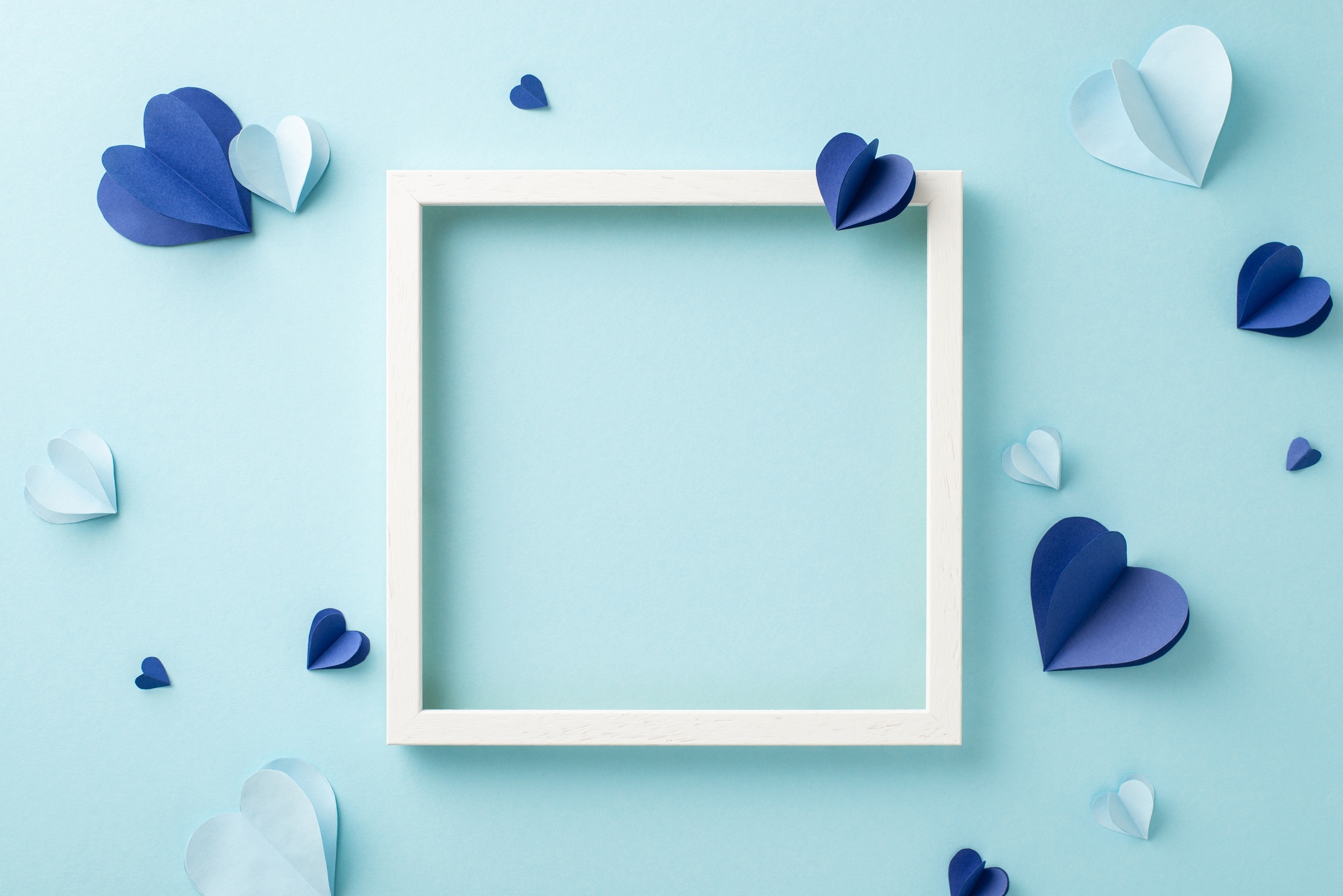 A creative flat lay with paper hearts and an empty frame arranged on a soft blue backdrop